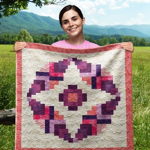 Puede incluir: Una mujer sostiene una colcha con un patrón geométrico en tonos rosa, morado y blanco. La colcha está acolchada con un diseño de espiral.