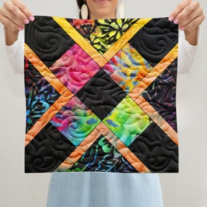 May include: A colorful quilt with a black background and a diamond pattern. The quilt is made of different fabrics with tie-dye and floral patterns. The quilt is edged with a yellow and orange border.
