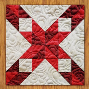 Puede incluir: Un bloque de colcha rojo y blanco con un diseño de estrella. La estrella está hecha de triángulos rojos y el fondo es blanco con un patrón de espiral.