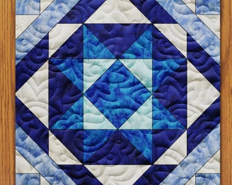 May include: A quilt block with a blue and white star pattern. The star is made up of triangles and squares, and the background is a white fabric with a blue swirl pattern.