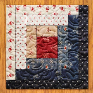 May include: A square quilt block with a log cabin design. The centre is red, surrounded by beige, blue, and white patterned fabrics. The fabrics feature floral and star patterns. The quilt block is on a wooden surface.