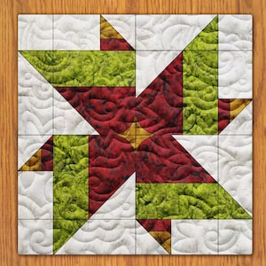 May include: A red, green, and gold quilt block with a pinwheel design. The block is made of fabric squares sewn together to create a geometric pattern.