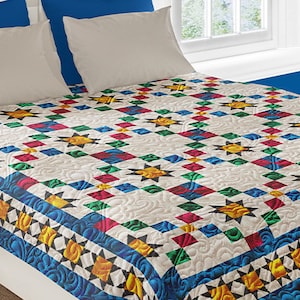 Könnte beinhalten: Eine weiße Bettdecke mit einem farbenfrohen geometrischen Muster. Die Bettdecke besteht aus Quadraten und Sternen in Rot-, Grün-, Blau- und Gelbtönen. Die Bettdecke liegt auf einem Bett mit blauen und weißen Kissen.