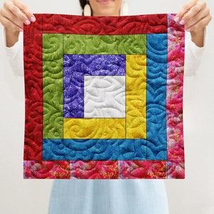 Op de afbeelding: Een kleurrijk quilt met een vierkant patroon in tinten rood, groen, blauw, geel en wit. De quilt is gemaakt van stof met een bloemenpatroon.