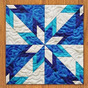 Könnte beinhalten: Eine blaue und weiße Steppdecke mit einem geometrischen Sternmuster. Die Steppdecke ist aus Stoff mit einem wirbelnden Muster und mit weißem Garn gesteppt.