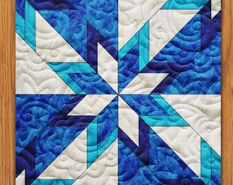 May include: A blue and white quilt with a geometric star pattern. The quilt is made of fabric with a swirling pattern and is quilted with white thread.