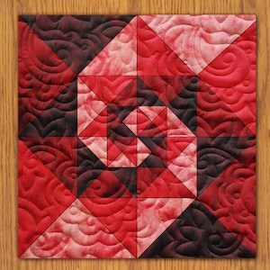 May include: A red and black quilt with a geometric pattern. The quilt is made of squares and triangles, and the pattern is repeated throughout the quilt.