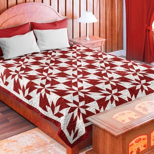 May include: A red and white quilt with a geometric pattern is on a bed with red and white pillows. The bed is in a room with wooden walls and a wooden chest at the foot of the bed.