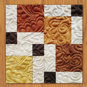 May include: A quilt made of nine squares with different patterns and colours. The squares are arranged in a 3x3 grid. The colours are brown, white, and yellow. The patterns are swirls and leaves.