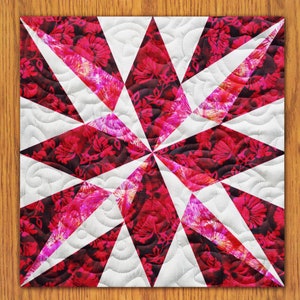 May include: A white and pink quilt with a starburst pattern. The quilt is made of fabric with a floral print.