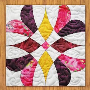 May include: A quilt block with a geometric design featuring curved shapes in shades of pink, purple, and yellow on a white background.