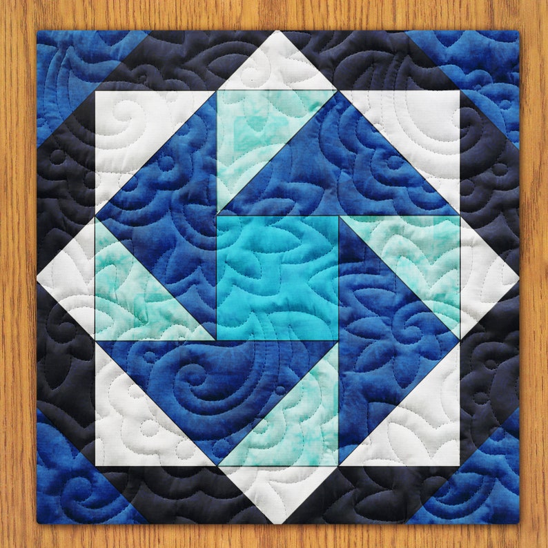 May include: A quilt block with a geometric design featuring a central blue square surrounded by white and blue triangles. The background is a dark blue fabric with a swirling pattern.