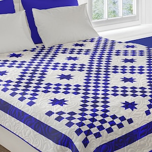 Könnte beinhalten: Eine weiße und blaue Bettdecke mit einem Rautenmuster und blauen Sternen. Die Bettdecke liegt auf einem Bett mit blauen und weißen Kissen.