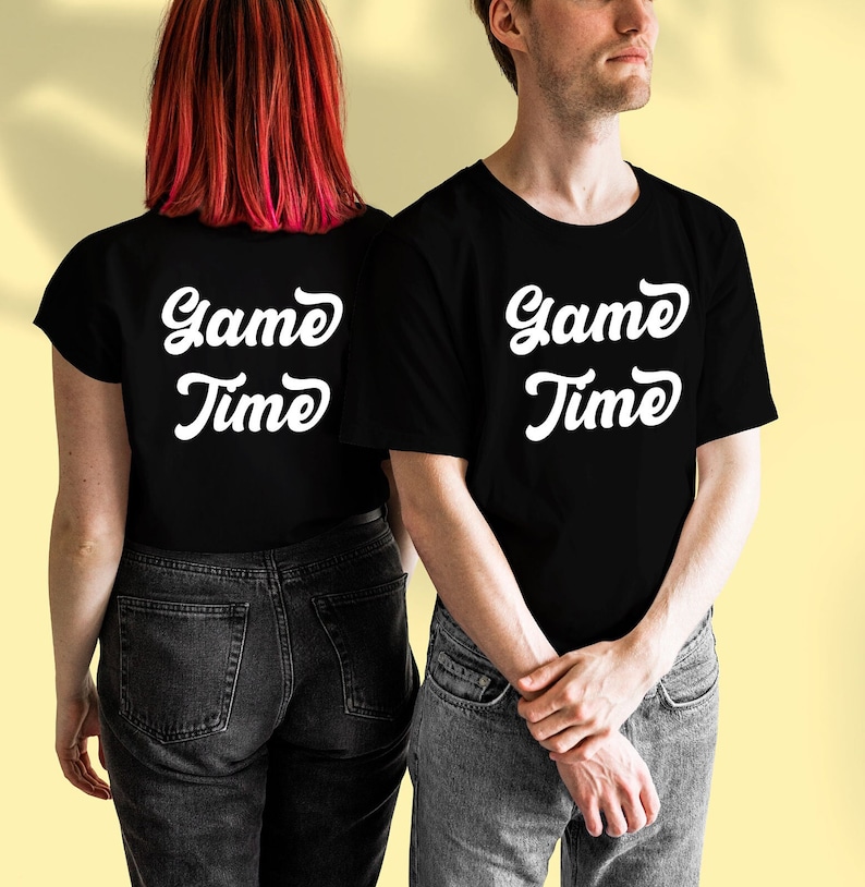 May include: Two people wearing black t-shirts with the text "Game Time" in white. The person on the left is wearing a black t-shirt with the text on the back. The person on the right is wearing a black t-shirt with the text on the front.