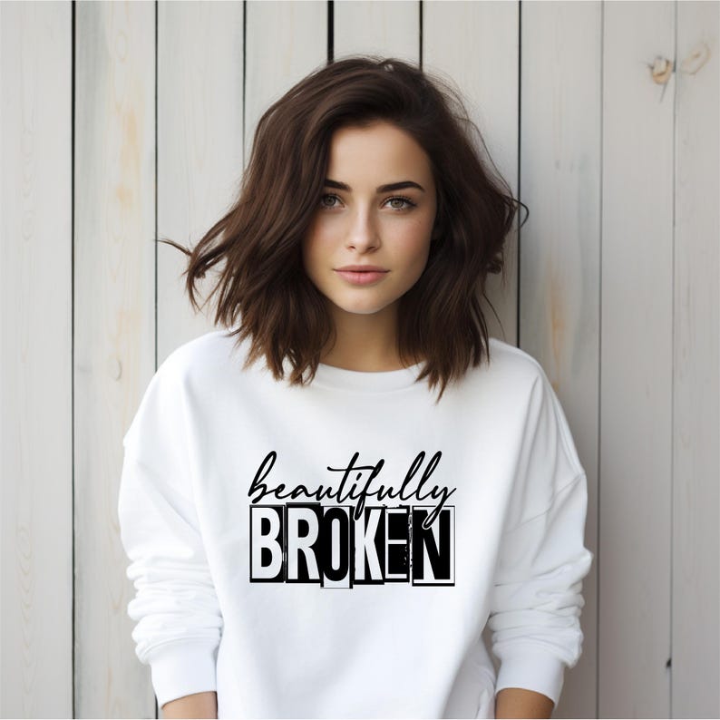 Pu&ograve; includere: Felpa bianca con la scritta "beautifully broken" stampata in nero. Il testo &egrave; in grassetto, in un carattere a blocchi.