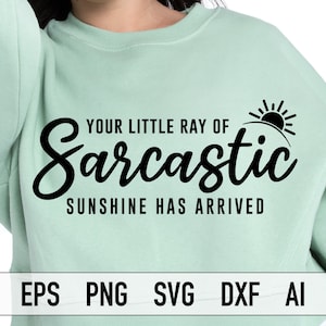 May include: A light green sweatshirt with the text "Your little ray of sarcastic sunshine has arrived" in black lettering. A small sun graphic is above the text.