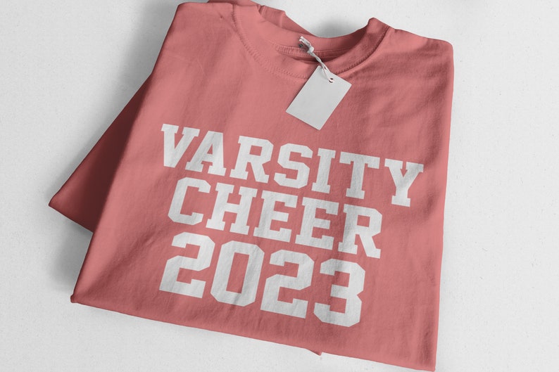 May include: A pink t-shirt with the text "VARSITY CHEER 2023" in white.