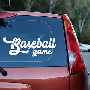 May include: A red car with a white vinyl decal on the back window that says "Baseball game".