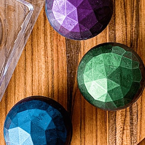May include: Three round, faceted, decorative ornaments in purple, green, and blue.