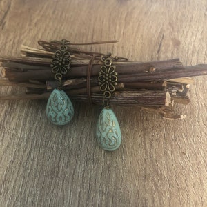 Peut inclure: Une paire de boucles d'oreilles pendantes avec une perle en forme de larme bleu sarcelle et un motif floral bronze.