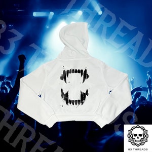 Könnte beinhalten: Weißer, kurzer Hoodie mit einem schwarzen Grafikdruck von Zähnen auf der Rückseite.