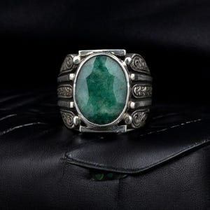 May include: A silver ring with an oval-shaped green gemstone set in a decorative silver band.