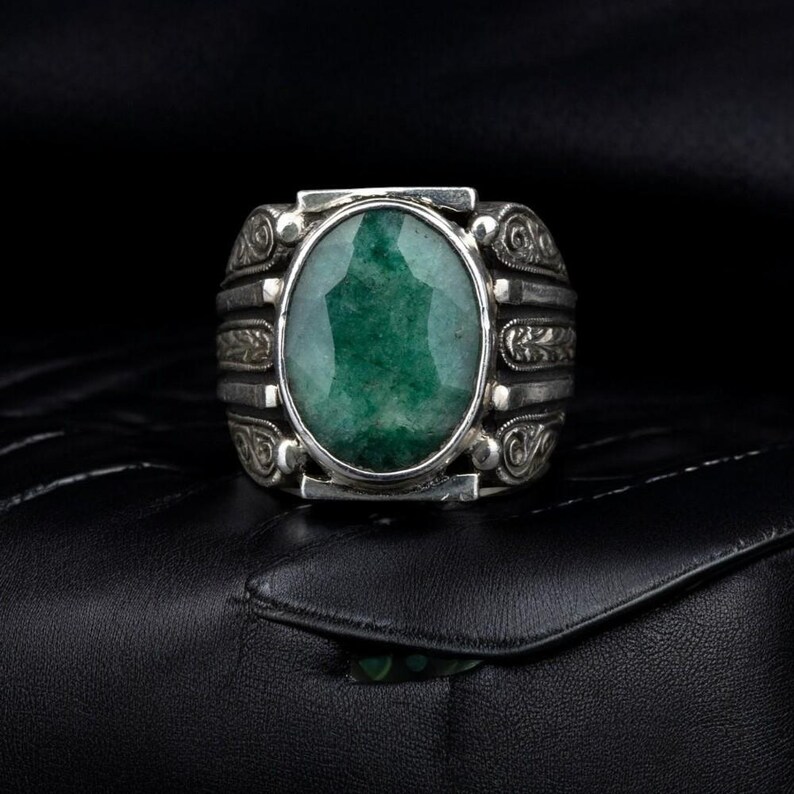 May include: A silver ring with an oval-shaped green gemstone set in a decorative silver band.