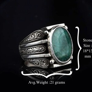 May include: A silver ring with an oval-shaped green gemstone. The ring has intricate floral designs on the band. Stone Size: 18*13 mm. Avg. Weight: 21 grams.