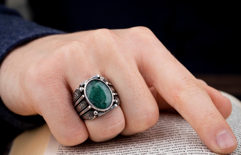 May include: A silver ring with an oval-shaped green gemstone set in a detailed silver band.