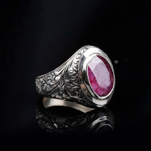 Può includere: Un anello d'argento con un designo floreale ornato e una grande pietra preziosa di rubino di forma ovale.