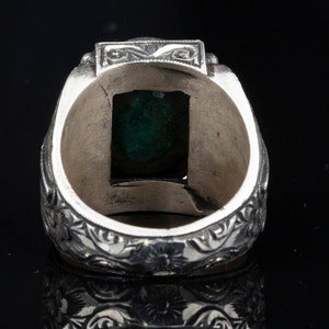 May include: A silver ring with an ornate design and a green gemstone set in the center.