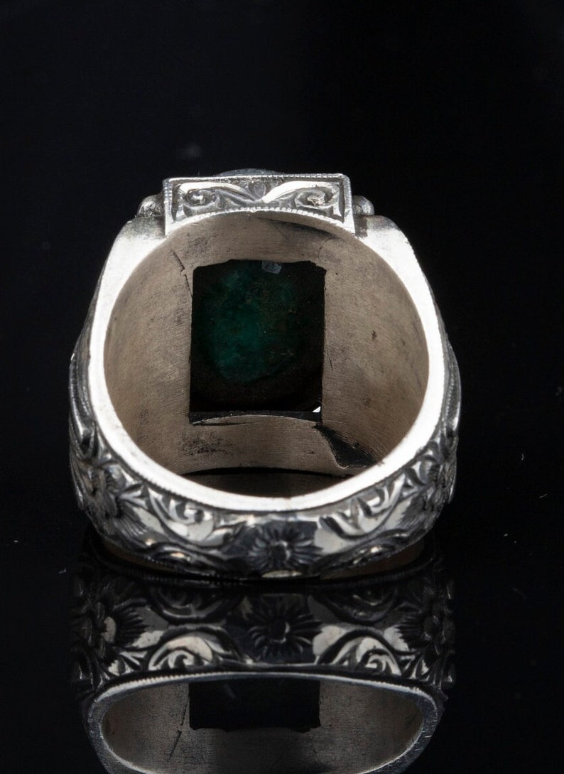 May include: A silver ring with an ornate design and a green gemstone set in the center.