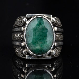 May include: A silver ring with an ornate design and a large, oval-shaped green gemstone.