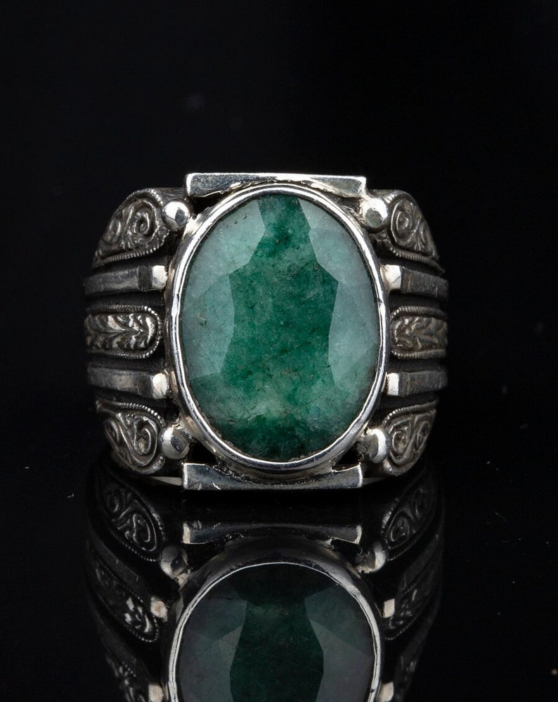 May include: A silver ring with an ornate design and a large, oval-shaped green gemstone.
