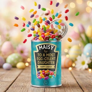 Puede incluir: Una lata turquesa de gominolas con el nombre "MAISY" y el texto "TO A MOST EGG-CELENT DAUGHTER HAPPY EASTER". La lata está llena de gominolas de colores, algunas de las cuales flotan en el aire. El fondo está borroso con decoraciones de Pascua.