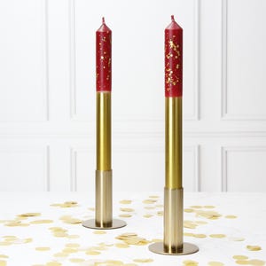 Può includere: Due candele rosse con glitter dorati incorporati nella cera. Le candele sono su portacandele in metallo dorato con base rotonda.