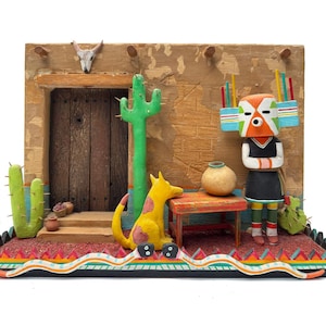 May include: A detailed diorama featuring a Southwestern theme. It includes a wooden door, a green cactus, a yellow dog, a small table with a pot, and a Native American Kachina doll. The base has a colorful, patterned design.