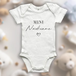 Könnte beinhalten: Weißer Baby Strampler mit schwarzem Text "MINI Nachname" und einem kleinen Herzsymbol.