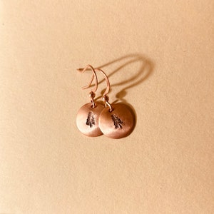 May include: A pair of copper dangle earrings with a small tree design on each disc.