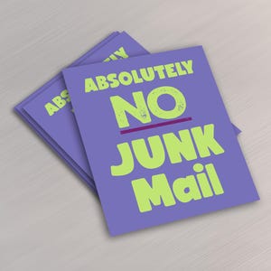 May include: A pile of purple rectangular cards with the words "ABSOLUTELY NO JUNK Mail" in lime green and purple. The cards are on a light wood-grain surface.