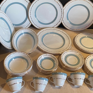May include: A set of white and blue china dinnerware with gold trim. The set includes plates, bowls, and teacups.