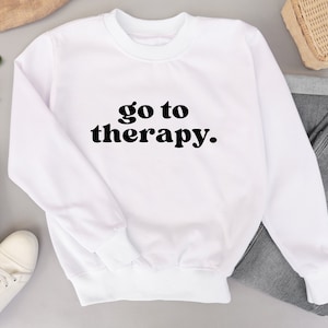 May include: White sweatshirt with the text "go to therapy." in black lettering.