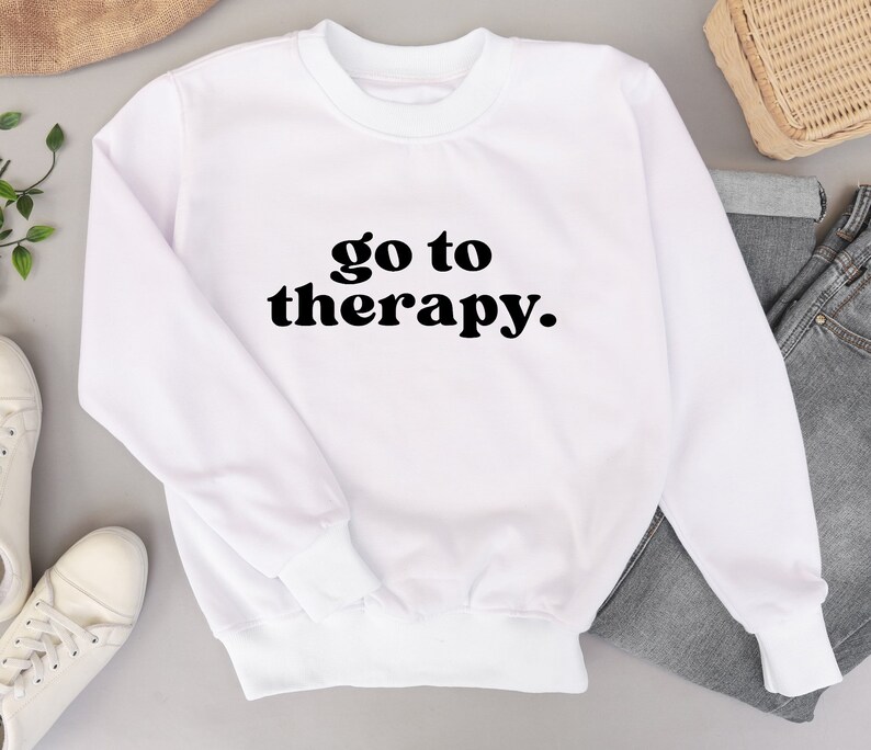 May include: White sweatshirt with the text "go to therapy." in black lettering.