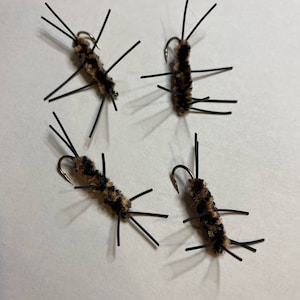 May include: Four brown and black fly fishing lures with black legs and gold hooks.