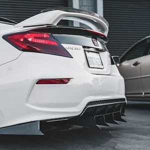 Peut inclure: Une Honda Civic blanche avec un aileron arrière noir et un diffuseur noir avec six ailettes. La voiture a des feux arrière teintés et un pare-chocs arrière noir.
