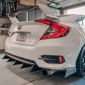 May include: A white Honda Civic with a large rear wing and a black diffuser with five fins. The car has a black number plate that reads "IC BLUE".