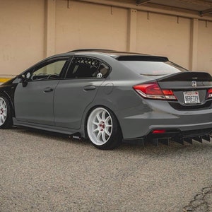 Peut inclure: Une Honda Civic berline grise avec un aileron arrière noir et des jantes après-vente. La voiture a une plaque d'immatriculation noire avec les lettres "8ERF729".