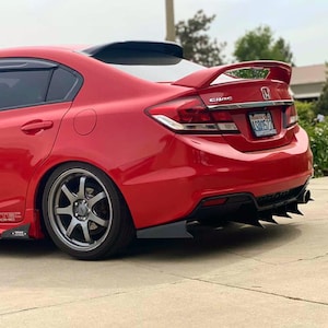 Peut inclure: Une berline Honda Civic rouge avec un aileron arrière et des détails noirs. La voiture a des jantes personnalisées et un pare-chocs arrière modifié avec des ailettes noires. La plaque d'immatriculation est visible.