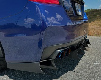 May include: A blue Subaru WRX with a black rear diffuser and a set of aftermarket exhaust tips. The car is parked on a tarmac surface.