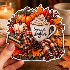 May include: A die-cut sticker featuring a white mug with the text Sweater Weather, topped with whipped cream and cinnamon sticks. The design includes orange and white pumpkins, a plaid bow, stacked books, a pinecone, acorns, and a plaid scarf.